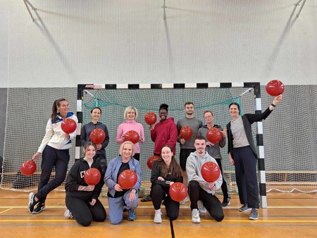 Gruppenbild der Teilnehmenden vor einem Handballtor in einer Sporthalle.