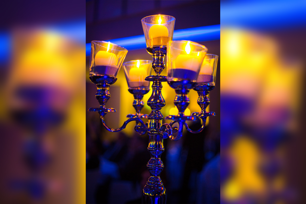 Nahaufnahme eines Metall-Kerzenleuchters mit gelben Kerzen vor dunkellauem Hintergrund.